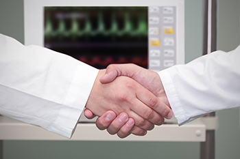 Two physicians shaking hands in front of an ECG machine