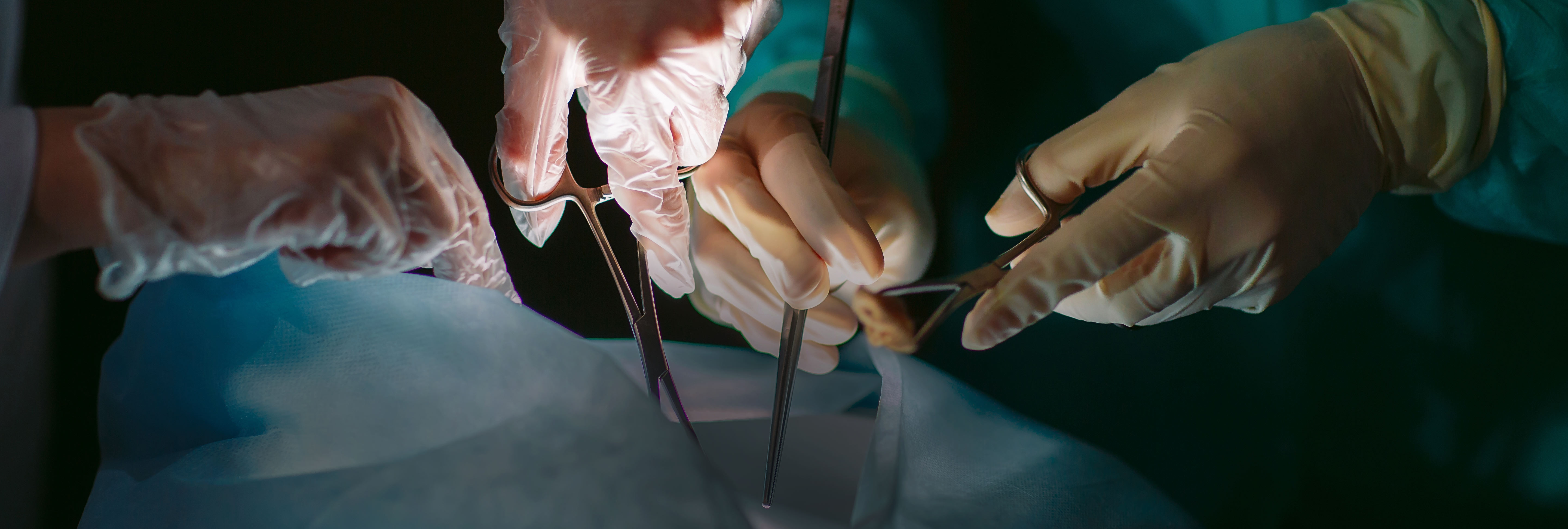 Medical procedure underway with one set of hands and an additional hand holding scissors and other medical tools