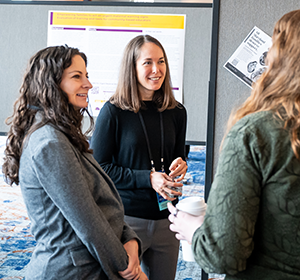 Two women are standing and speaking to each other in a conference like setting.