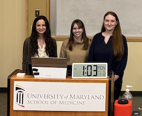 Three women stand behind a podium that reads university of maryland school of medicine