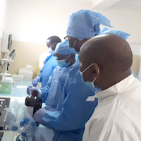 Several people wearing blue lab protective gear huddle together in a lab.