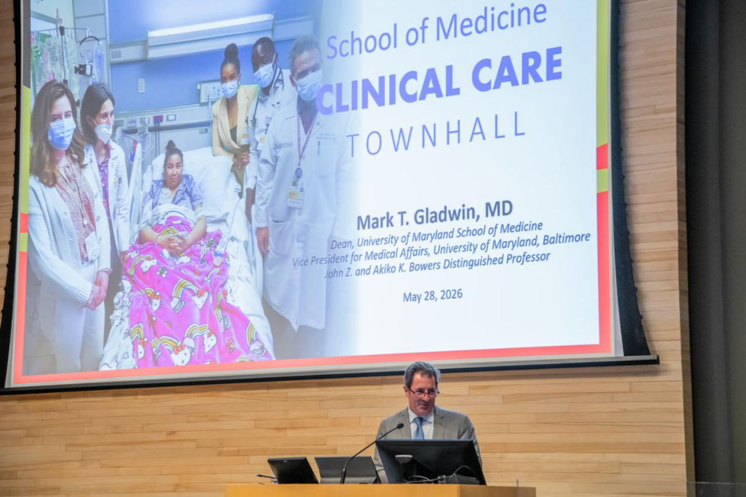 Dean Gladwin speaking at a podium with a screen behind him with the text 'School of Medicine Clinical Care Town Hall'