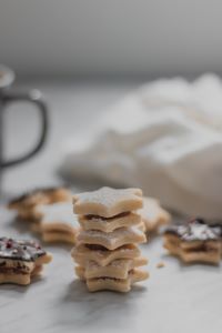 A stack of star shaped sugar cookies on a marble countertop with the handle of a mug and some frosting in the background
