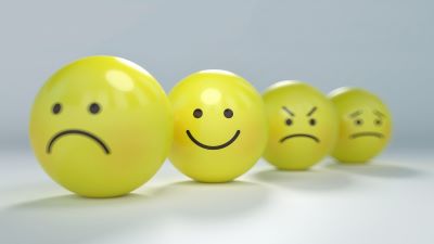 Four yellow balls with black faces drawn on them in marker. The front face is a frown, the second face is a smile, the third face is angry, and the fourth face is worried.