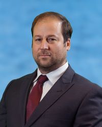 Photo of Dr. James Borrelli in a black suit jacket, white shirt, and red tie on a blue background