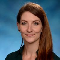 Photo of Katrina Williams, PhD in a black shirt on a blue background