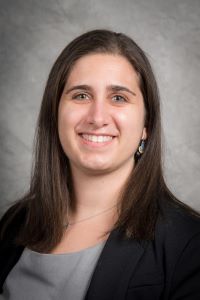 Cali Calarco, PhD in black blazer and gray top against a gray background