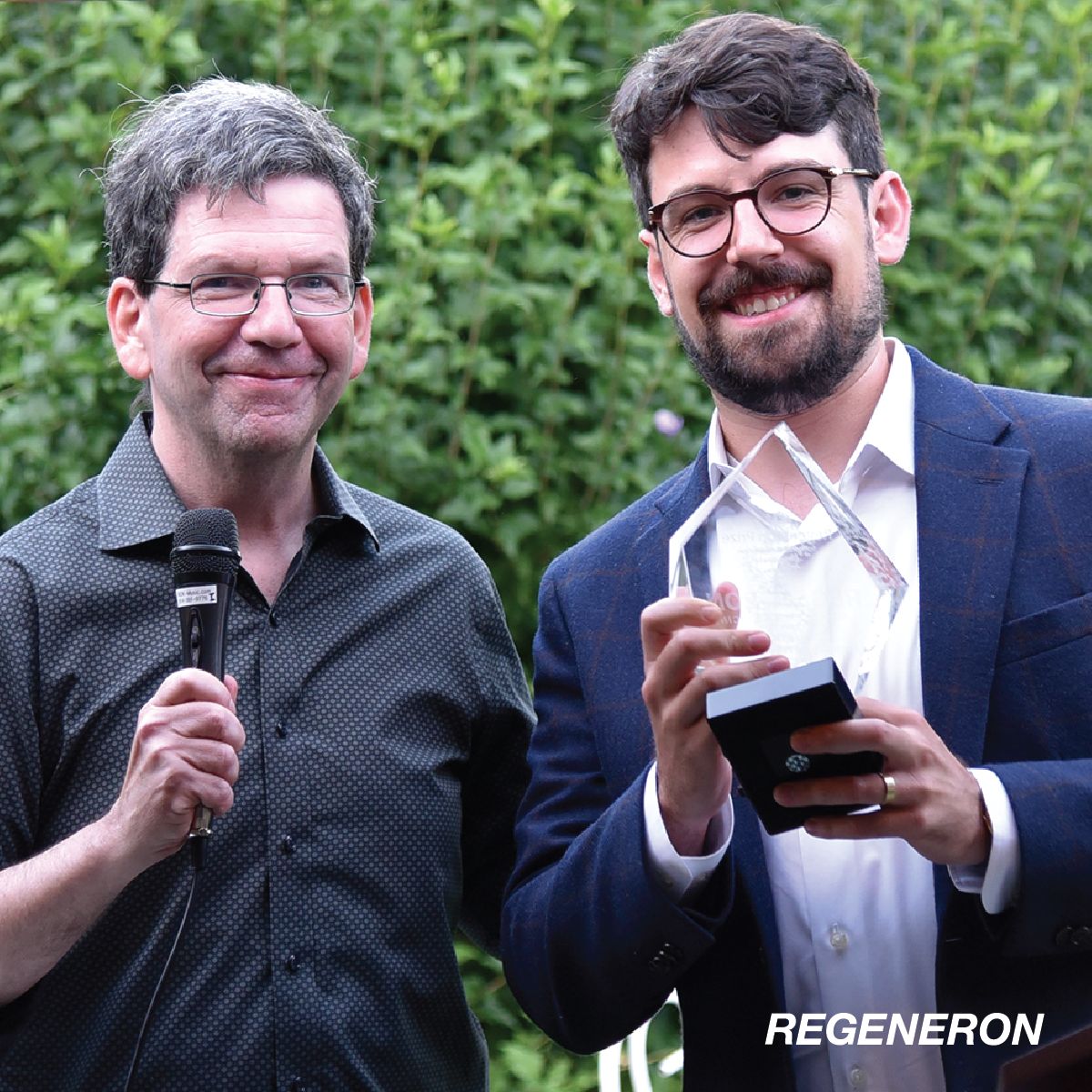 Photo of Dr. Sam Barlow holding a diamond shaped award and standing next to another man holding a microphone