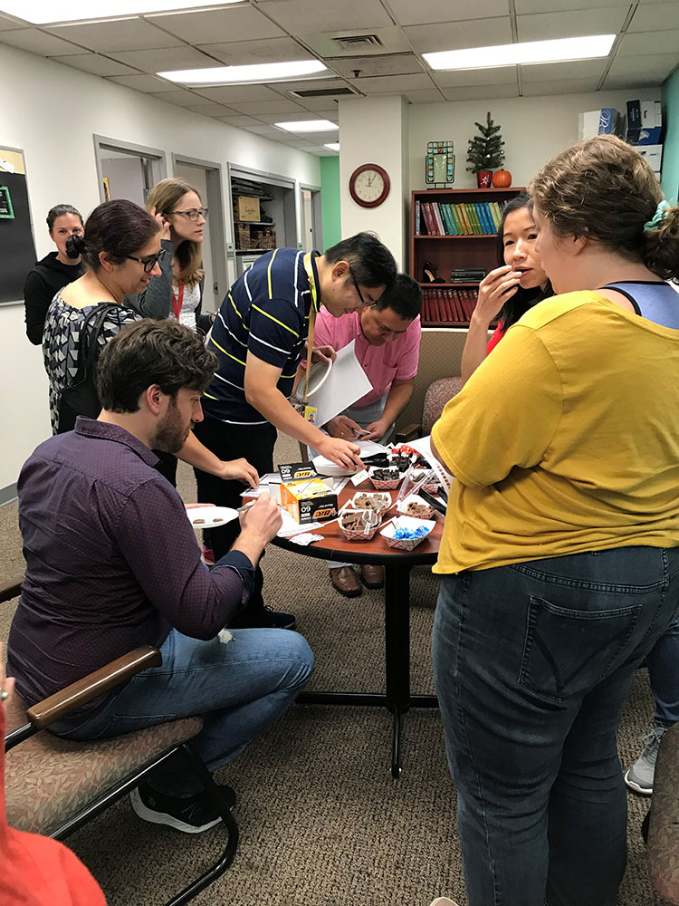 Adults standing around a table with sliced chocolate and pens