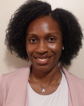 Student headshot. Woman standing in front of a light colored wall wearing a white shirt with a light pink sweater.